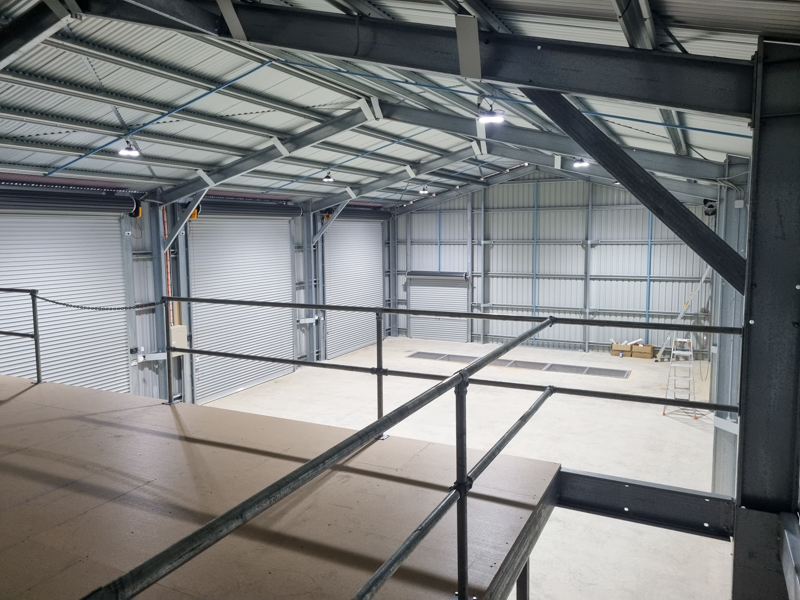 Interior of a custom shed viewed from the mezzanine, showing steel framing and different sized roller doors